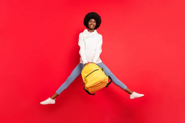 Full length photo of funny brunette millennial lady jump with bag wear hoodie jeans isolated on red background — Stock Photo, Image