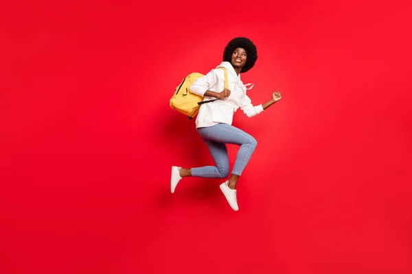 Full size φωτογραφία προφίλ του εντυπωσιασμένος κυματιστό hairdo φοιτήτρια κυρία τρέχει με σακίδιο φορούν λευκό αθλητικά τζιν απομονωμένο σε κόκκινο χρώμα φόντο — Φωτογραφία Αρχείου