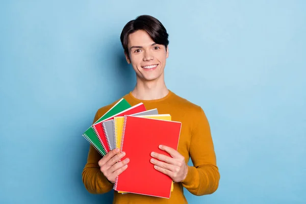 Foto de un buen moreno joven sostiene libros usa suéter marrón aislado sobre fondo de color azul —  Fotos de Stock