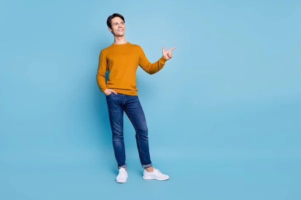 Foto av promotor killen ange pekfinger tomt utrymme bära orange skjorta jeans skor isolerad blå färg bakgrund — Stockfoto