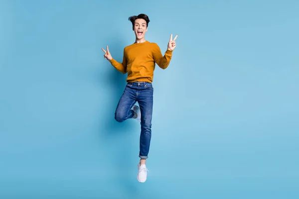 Foto de comprimento total de cool morena jovem salto mostra v-sign desgaste camisola jeans isolado no fundo de cor azul — Fotografia de Stock