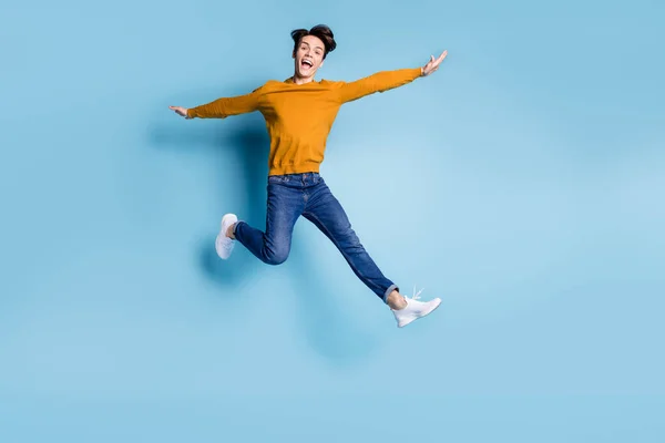 Foto de comprimento total de alegre morena jovem cara salto gritar desgaste camisola jeans isolado no fundo de cor azul — Fotografia de Stock