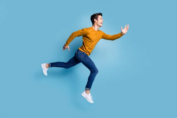 Volledige lengte profiel foto van grappige brunet jonge man run slijtage trui jeans geïsoleerd op blauwe kleur achtergrond — Stockfoto