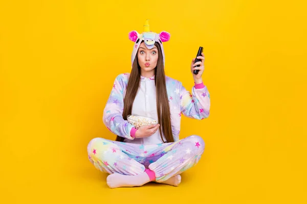 Portrait of attractive amazed girl sitting watching film wearing cozy kingurumi isolated over bright yellow color background — Stock Photo, Image