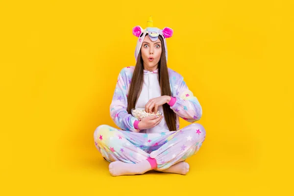 Portrait of attractive amazed girl sitting lotus pose eating corn watching series isolated over bright yellow color background — Stock Photo, Image