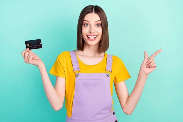 Фото изумленной счастливой брюнетки Боб с волосами женщины указывать пальцем пустое пространство кредитная карта изолированы на бирюзовом фоне — стоковое фото