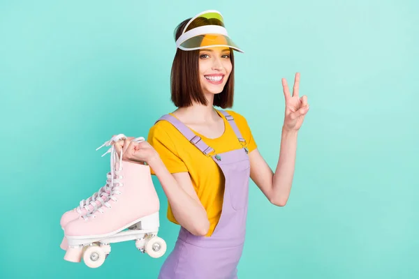 Foto de la encantadora joven agradable mujer usar sombrero de tenis mantenga patines muestran v-signo aislado sobre fondo de color verde azulado — Foto de Stock