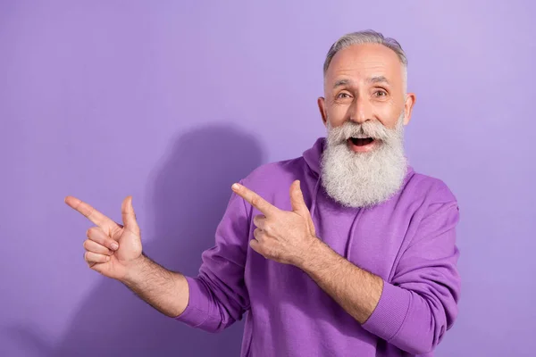 Retrato de un atractivo anciano retirado de moda hombre de pelo gris mostrando espacio en blanco de copia aislado sobre fondo violeta violeta — Foto de Stock