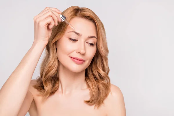 Retrato de mulher sonhadora atraente aplicando soro bio hialurônico na testa isolada sobre fundo de cor pastel cinza — Fotografia de Stock