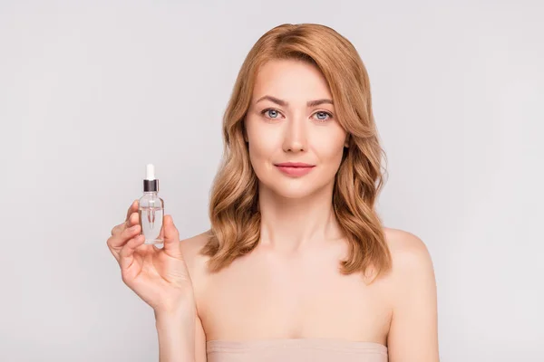 Portrét atraktivní ženy drží v ruce sérum láhev inzerovat nový bio produkt izolované přes šedé pastelové barvy pozadí — Stock fotografie