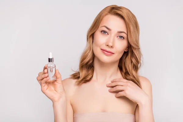 Portrait of attractive woman holding in hand cosmetic facial oil bottle bio product isolated over grey pastel color background