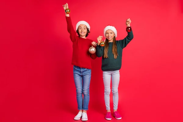 Foto van positieve charmante schoolkinderen dragen gebreide truien met kerst ballen glimlachen geïsoleerde rode kleur achtergrond — Stockfoto