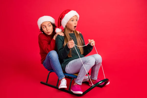 Foto av glada chockade skolbarn klädda stickade tröjor ridning slädar ser tomt utrymme isolerad röd färg bakgrund — Stockfoto