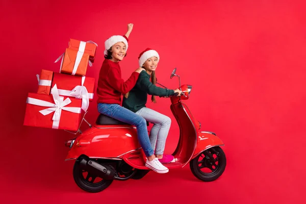 Foto van grappige mooie schoolkinderen gekleed gebreide truien rijden bromfiets met cadeautjes geïsoleerde rode kleur achtergrond — Stockfoto