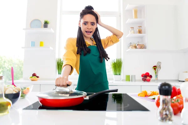 Фото потрясенной темнокожей женщины, одетой в желтую рубашку, которая готовит открывающуюся сковородку в доме — стоковое фото