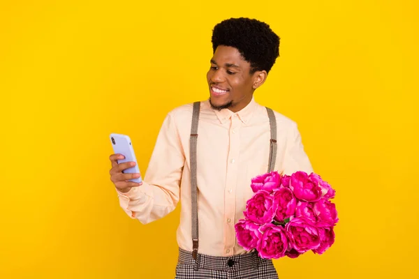 Foto ritratto uomo in camicia mantenere mazzo di fiori sulla festa di compleanno utilizzando smartphone isolato vivido colore giallo sfondo — Foto Stock