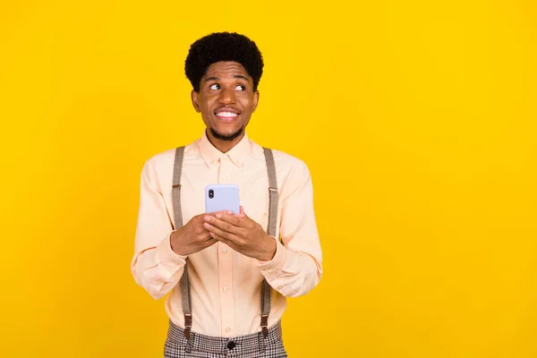 Foto di ispirato premuroso ragazzo tenere telefono look spazio vuoto indossare bretelle camicia isolato colore giallo sfondo — Foto Stock