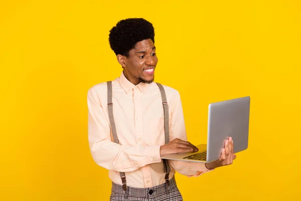 Foto de programador chico mantenga portátil mirada pantalla desgaste tirantes camisa aislado color amarillo fondo —  Fotos de Stock