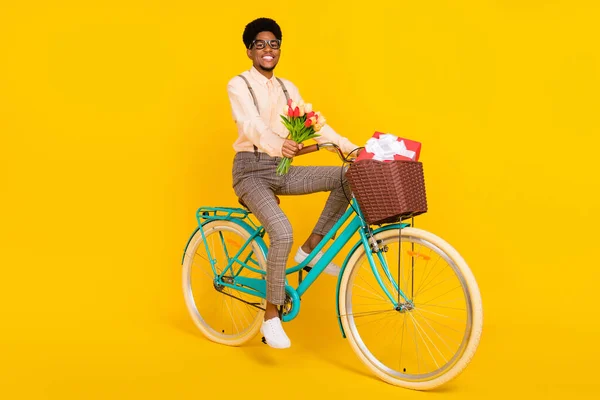 Фото веселого доглянутого хлопця, який їде на велосипеді, тримає квіти у підтяжці сорочки ізольованого жовтого кольору — стокове фото
