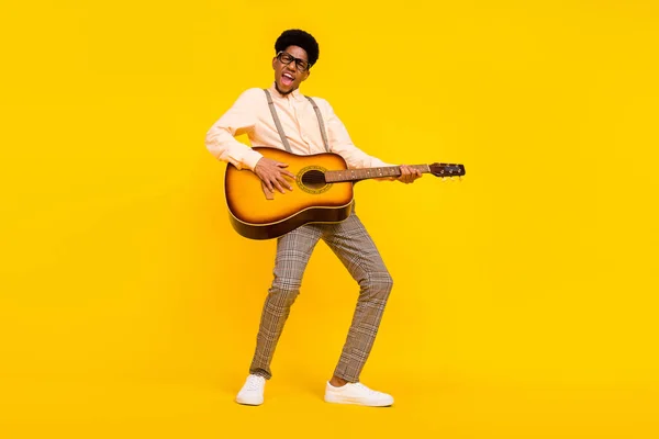 Foto de animador despreocupado sujeto guitarra juego composición desgaste tirantes camisa aislado color amarillo fondo — Foto de Stock