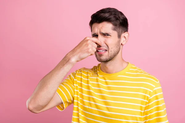 Portrét atraktivní depresivní pochmurný náladový chlap zavírání nosu špatný zápach izolované přes růžové pastelové barvy pozadí — Stock fotografie