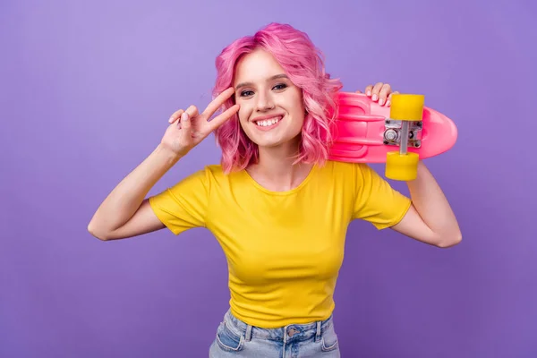 Foto von jungen fröhlichen Mädchen glücklich positives Lächeln zeigen Frieden cool V-Zeichen Skateboard isoliert über lila Farbhintergrund — Stockfoto