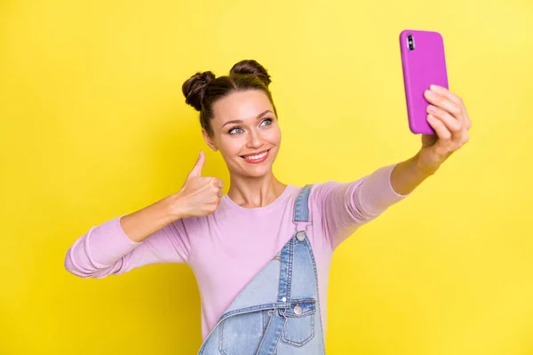 Foto de encantadora mujer linda desgaste denim general viraje selfie dispositivo moderno que muestra pulgar hacia arriba aislado color amarillo fondo —  Fotos de Stock