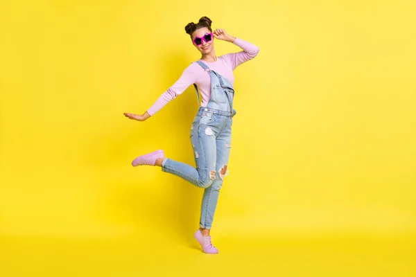 Foto av söt cool ung dam klädd jeans övergripande mörka glasögon dans isolerad gul färg bakgrund — Stockfoto