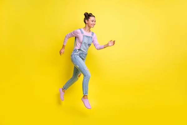 Profil foto av snabb dam hoppa springa ser tomt utrymme slitage denim övergripande skor isolerad gul bakgrund — Stockfoto