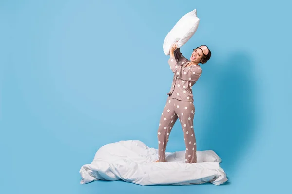 Foto em tamanho completo de jovem louca feliz sorrindo menina em pijama travesseiro luta sleepover isolado no fundo de cor azul — Fotografia de Stock