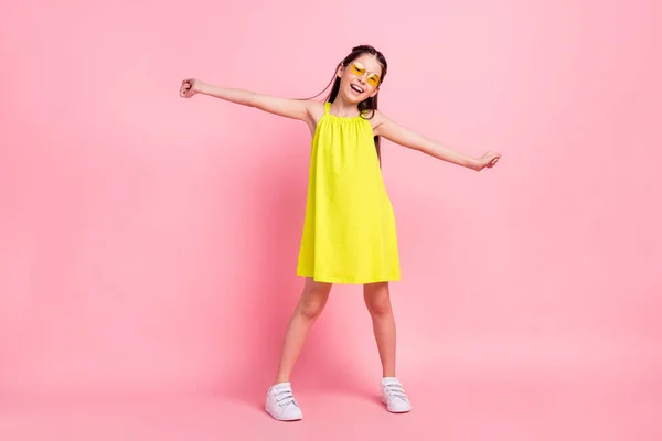 Full length foto di adorabile funky scuola ragazza indossare abito giallo occhiali sorridente ballando braccia lati isolato colore rosa sfondo — Foto Stock