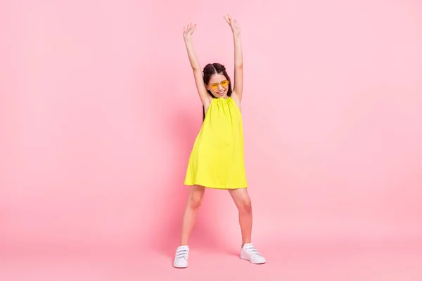 Foto de comprimento total de encantador bonito escola menina desgaste vestido amarelo óculos sorrindo dançando levantando braços isolado cor rosa fundo — Fotografia de Stock