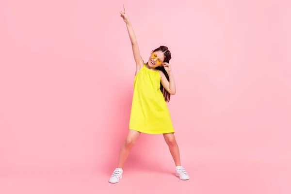 Volledige lengte foto van vrij grappig schoolmeisje gekleed gele outfit bril dansen wijzend lege ruimte geïsoleerde roze kleur achtergrond — Stockfoto