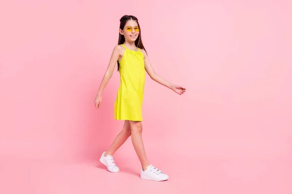 Full length φωτογραφία του χαριτωμένο γοητευτικό κορίτσι σχολείο φορούν κίτρινο φόρεμα σκούρα γυαλιά περπάτημα κενό χώρο απομονωμένο ροζ χρώμα φόντο — Φωτογραφία Αρχείου