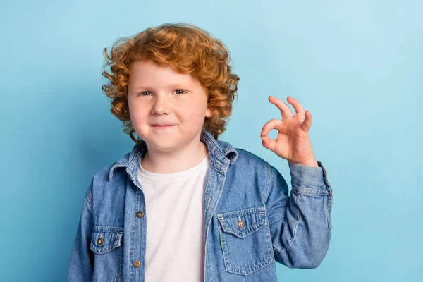 Photo de promoteur positif fiable petit garçon montrer okey geste porter jeans veste isolé fond de couleur bleue — Photo