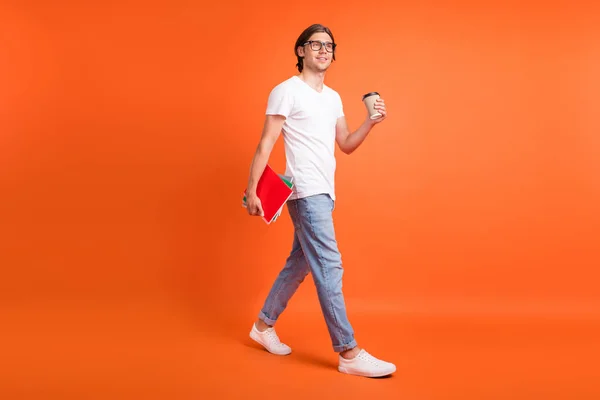 Full length photo of young dreamy happy man look go empty space hold note coffee isolated on orange color background — Stock Photo, Image