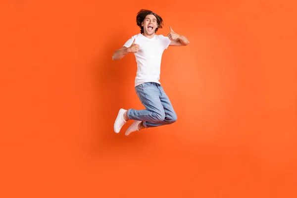 Full length φωτογραφία του νεαρού χαρούμενα θετικός άνθρωπος άλμα μέχρι δείχνουν τους αντίχειρες μέχρι χαμόγελο απομονώνονται σε πορτοκαλί χρώμα φόντο — Φωτογραφία Αρχείου