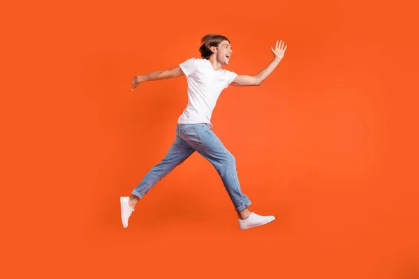 Foto sisi profil penuh dari pria muda yang bahagia dan ceria melompat pria berlari ruang kosong terisolasi pada latar belakang warna oranye — Stok Foto