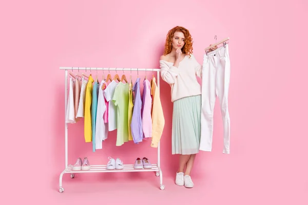 Pełna długość zdjęcie młodej dziewczyny myśleć wybór wygląd spodnie ubrania zakupy izolowane na różowy kolor tła — Zdjęcie stockowe