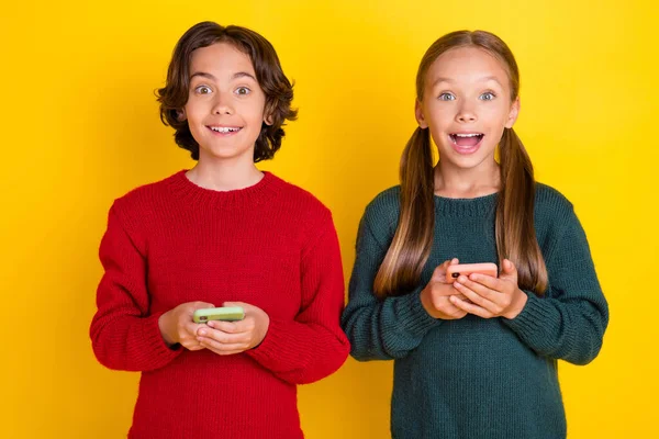 Foto retrato dos niños sorprendidos usando teléfonos inteligentes aislados vívido color amarillo fondo —  Fotos de Stock