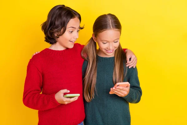 Retrato de dos hermosos amigos alegres guapos abrazándose usando el dispositivo de chat aislado sobre fondo de color amarillo brillante —  Fotos de Stock