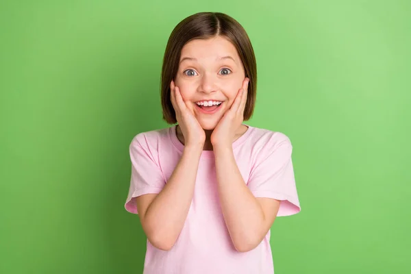 Foto de menina pequena feliz sorriso positivo surpreendido chocado surpreendido mãos toque bochechas isoladas sobre fundo de cor verde — Fotografia de Stock