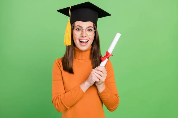 Retrato de menina alegre atraente usando mestres chapéu segurando papel scroll grau de bacharel isolado sobre fundo de cor verde — Fotografia de Stock