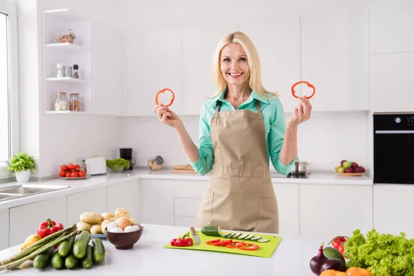 Fotografie de femeie atractivă matură zâmbet pozitiv fericit țineți felii de piper gătiți micul dejun legume alimente sănătoase dietă acasă Imagini stoc fără drepturi de autor