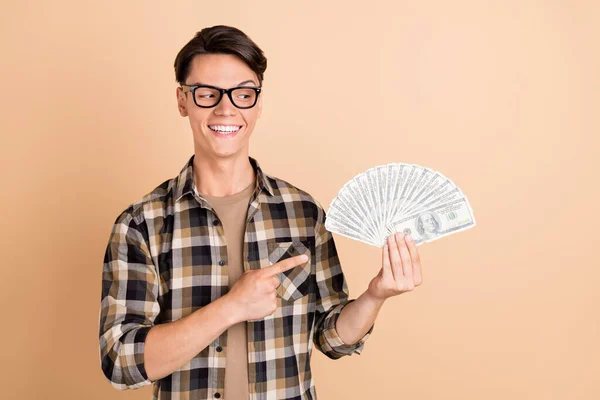 Foto van nieuwsgierige positieve man houden fan geld geven vinger kijken kant slijtage geruite shirt geïsoleerde beige kleur achtergrond — Stockfoto