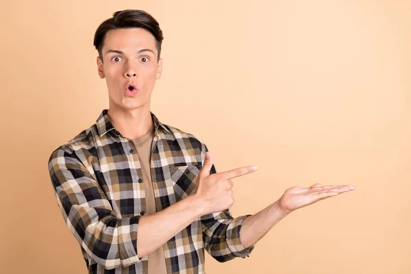 Foto de punto de chico milenario impresionado mantenga vacío el espacio use camisa a cuadros aislada sobre fondo de color beige — Foto de Stock