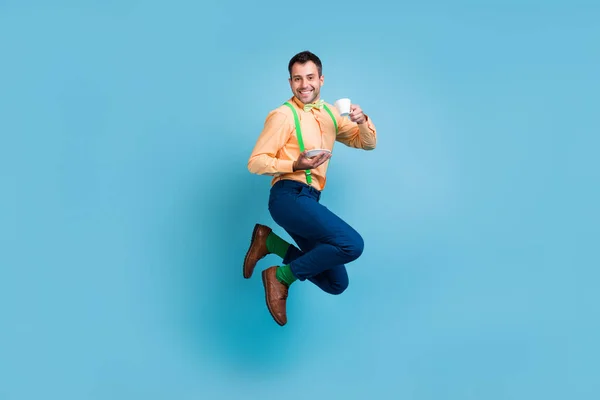 Foto de chico británico salto celebrar taza beber té desgaste tirantes camisa pantalones zapatos aislados color azul fondo —  Fotos de Stock