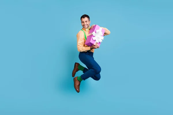 Foto di pazzo spensierato ragazzo salto tenere regalo pacchetto correre indossare bretelle camicia isolato colore blu sfondo — Foto Stock