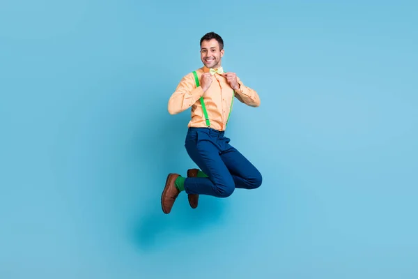 Фото красивого впевненого хлопця стрибати закріпіть краватку з бантом зубну посмішку підтяжки сорочки ізольований синій колір фону — стокове фото