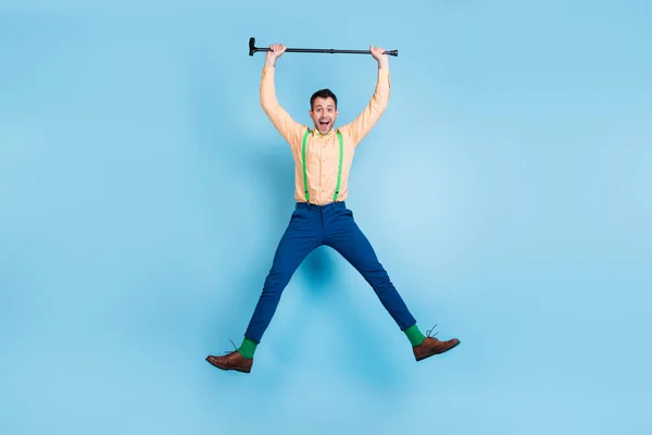 Foto di energico ragazzo salto tenere bastone da passeggio sollevare braccia indossare bretelle camicia papillon isolato colore blu sfondo — Foto Stock